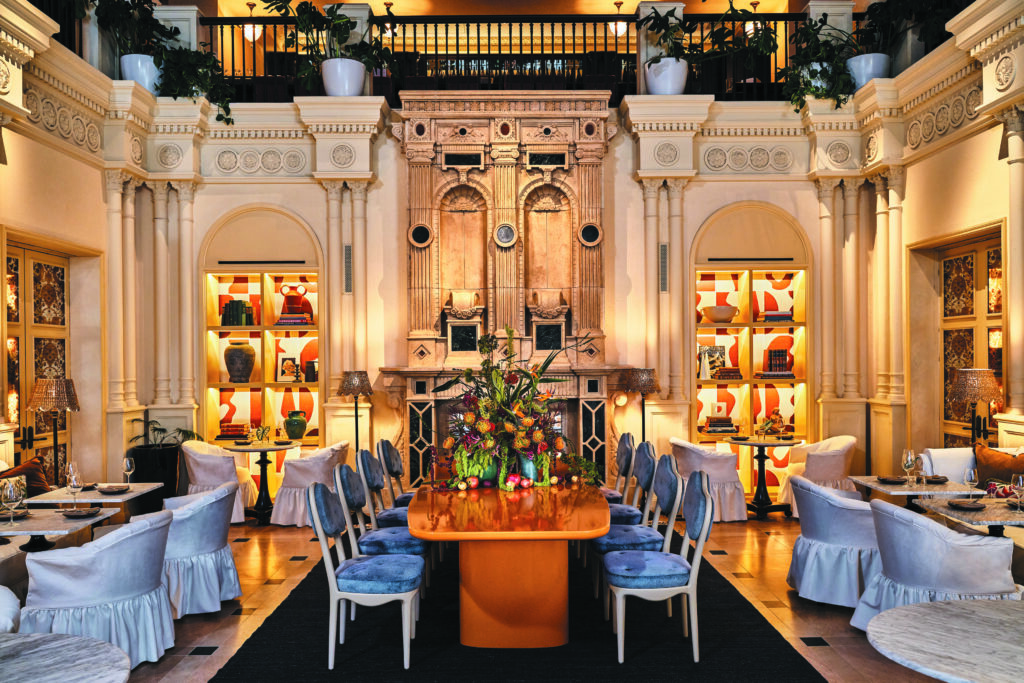 The custom communal table, fabricated by local artisans in a glossy marigold, and asymmetrical dining chairs, upholstered in a blue mohair whose color nods to the room’s coffered ceiling, are the only pieces of new furniture in the dining room. New wallpaper by Garance Vallée for Élitis animates the room’s bookcases. Photos by The Ingalls.